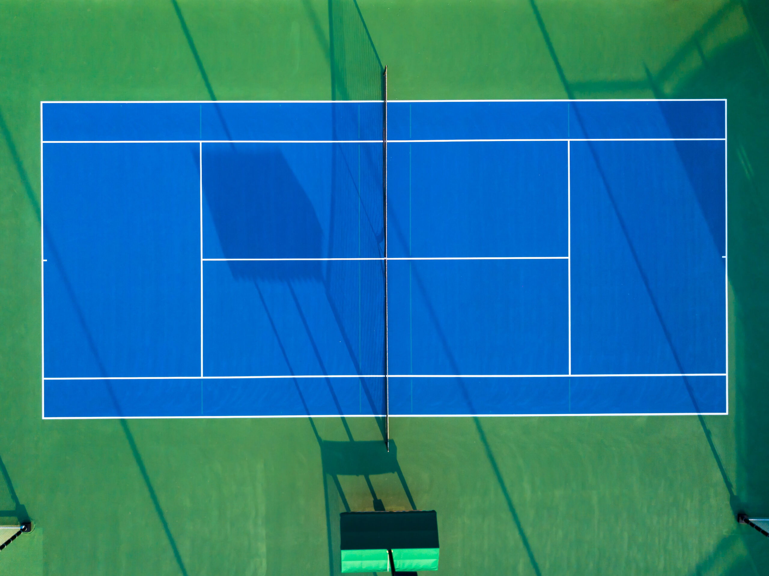 Drone shot capturing a vibrant blue tennis court from above, showcasing geometric patterns.
